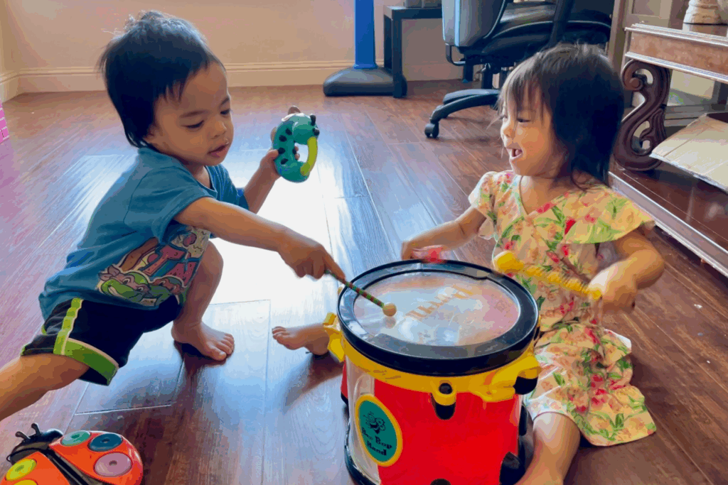 Two little kids sitting on the floor playing a drum together